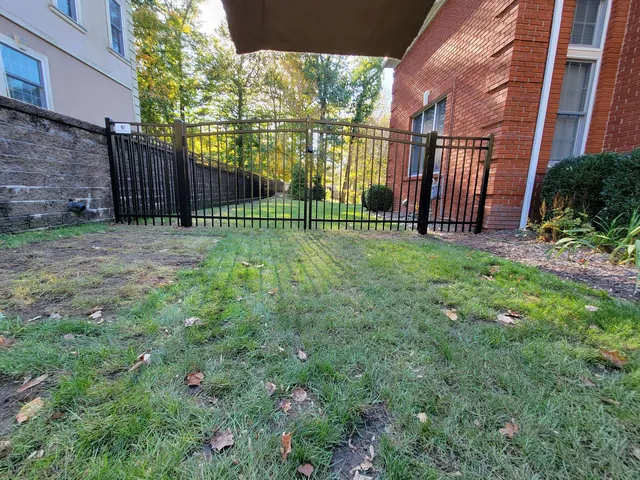Black aluminum fence with a double gate between a brick house and a stone wall, opening onto a lawn