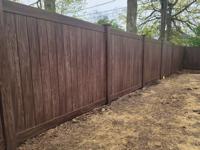 Brown woodgrain vinyl privacy fence running along newly strawed ground