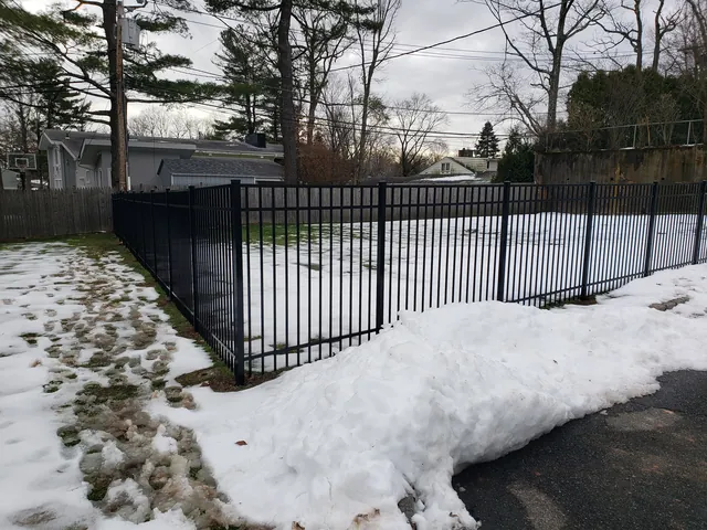 Black aluminum fence around a yard and along a driveway, with snow on the ground